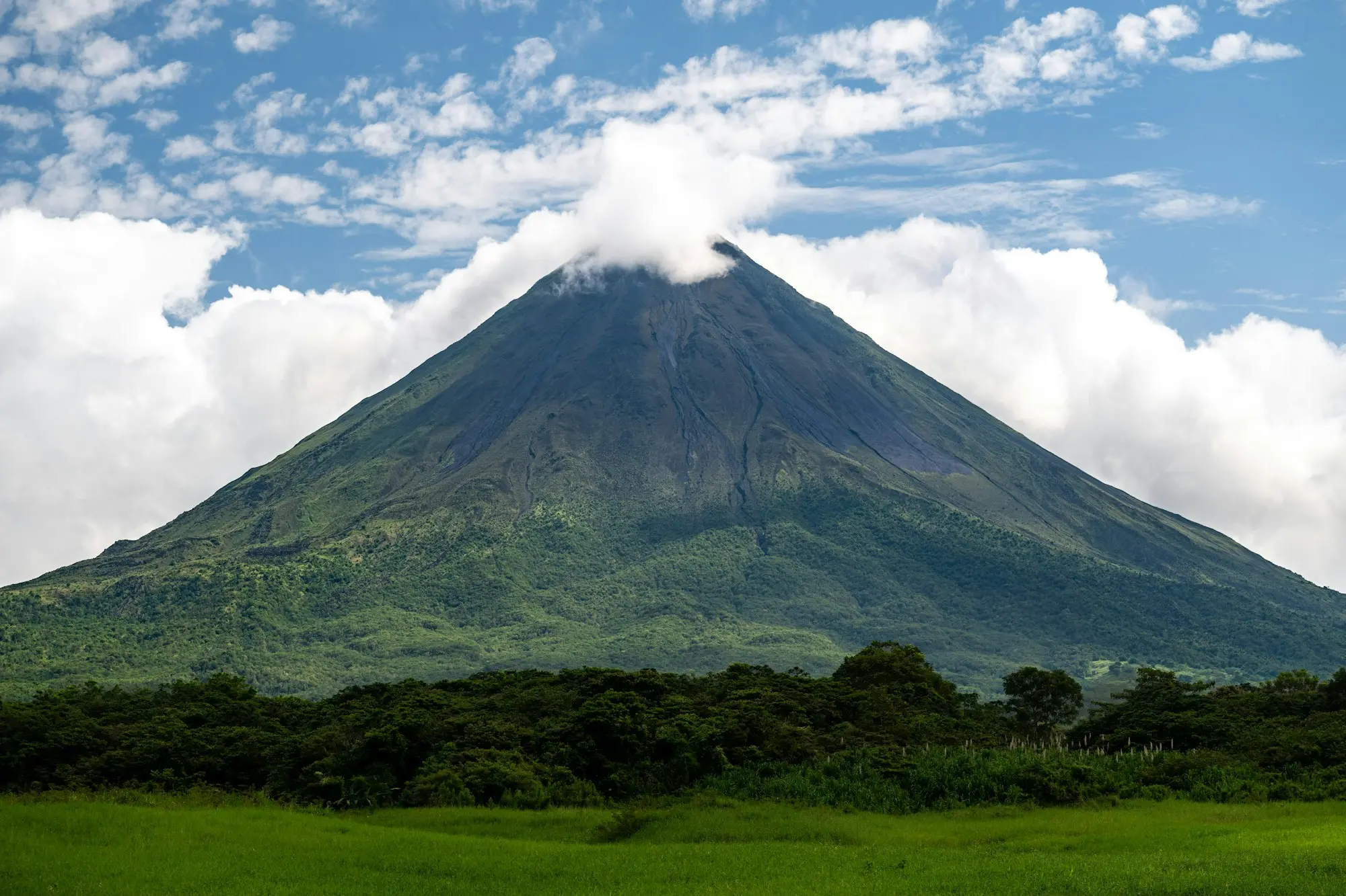 The green cone of Arenal volcano rising above forest and pasture under clouds in Costa Rica