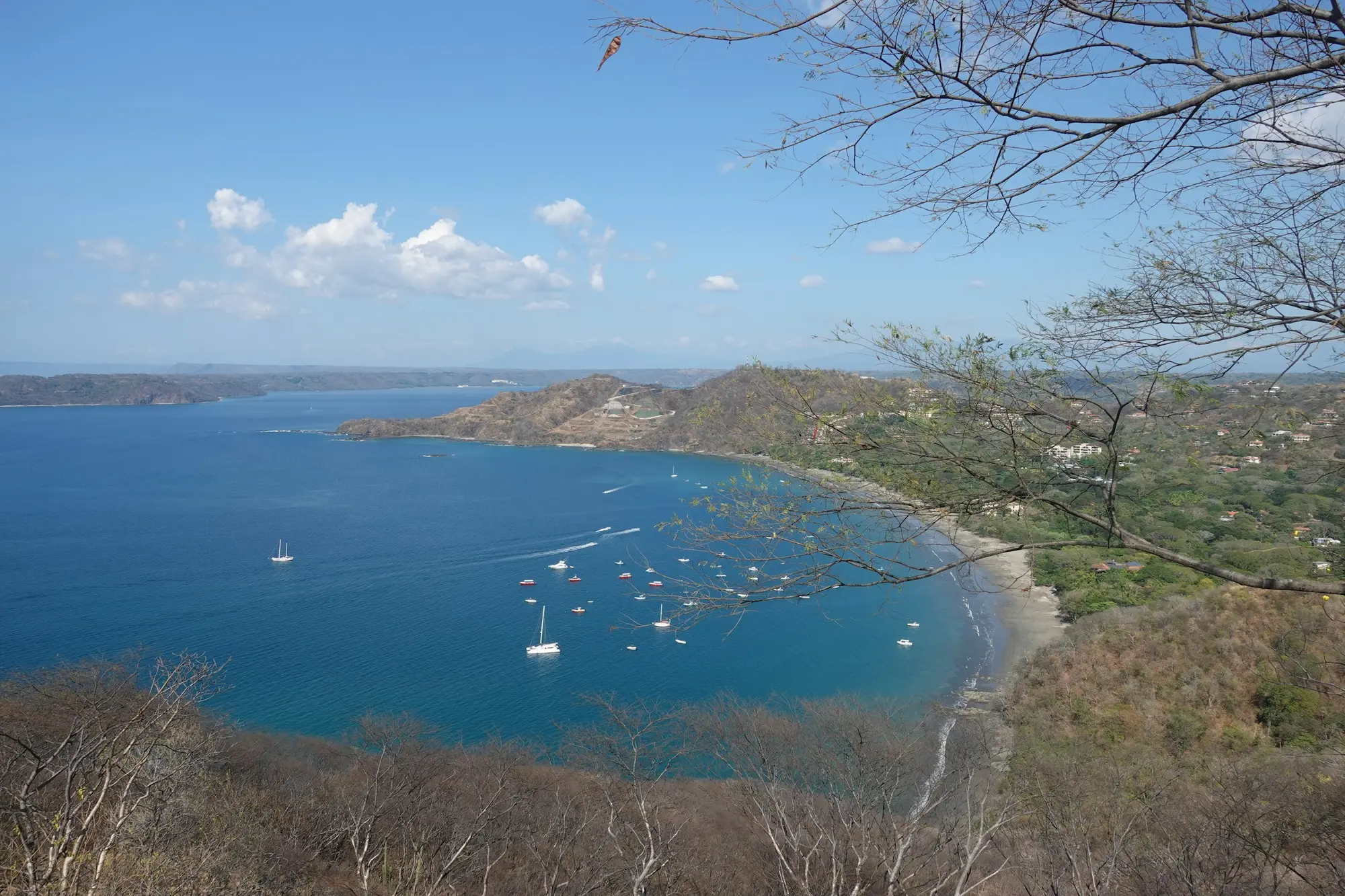 A calm Guanacaste bay with anchored boats seen from a dry-forest hillside